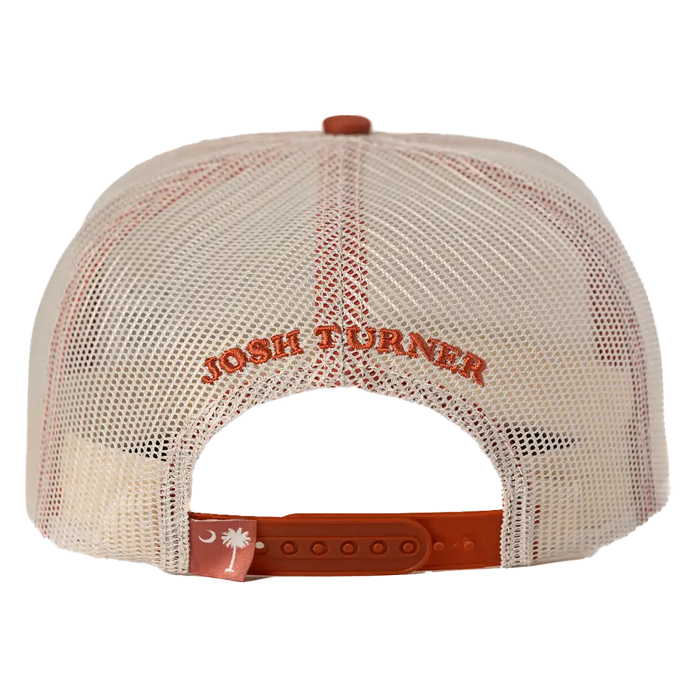 Cream-colored mesh trucker hat with orange embroidered ’josh turner’ text and a matching orange adjustable strap featuring a white crescent moon and palmetto tree logo.