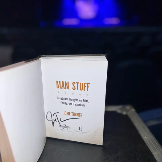 A signed hardcover copy of ’man stuff’ by josh turner, featuring orange text on a white page with the author’s signature below.