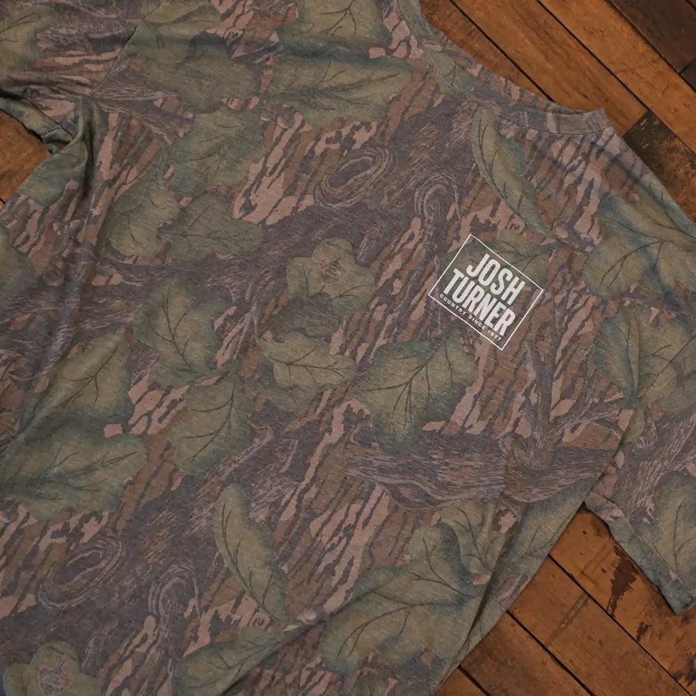 A camouflage-patterned josh turner t-shirt with a white rectangular logo on the chest.