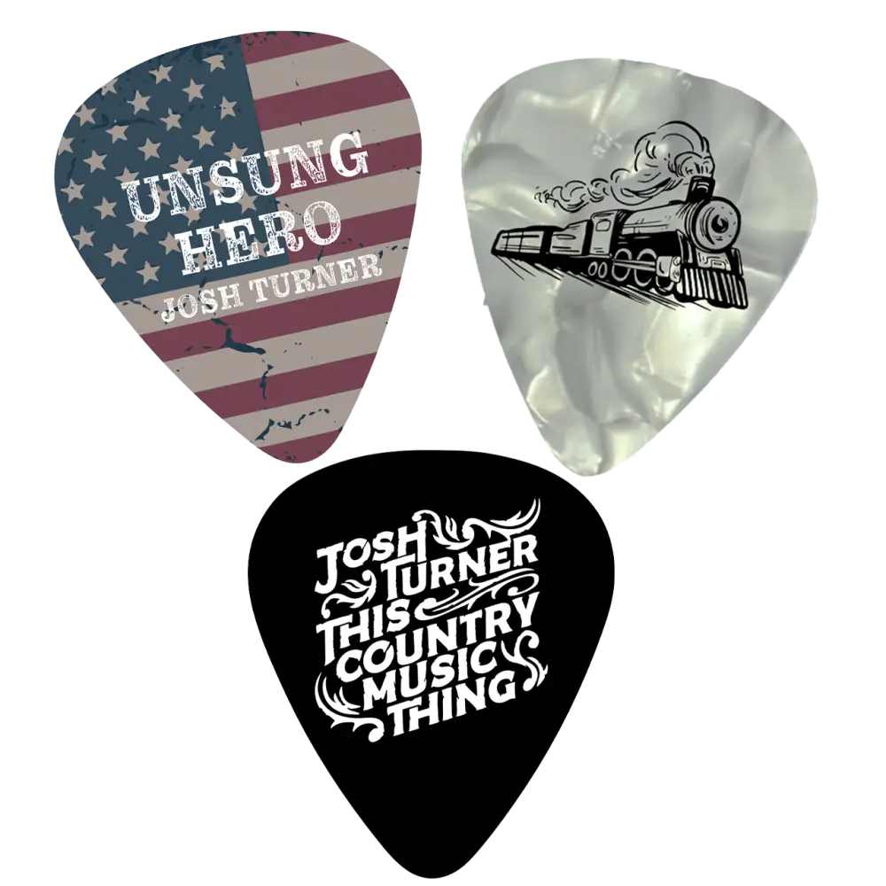 Three guitar picks featuring designs related to josh turner: one with a distressed american flag pattern, another translucent pearlescent pick with a black steam train illustration, and a solid black pick with white ornate lettering for ’this country music thing.’