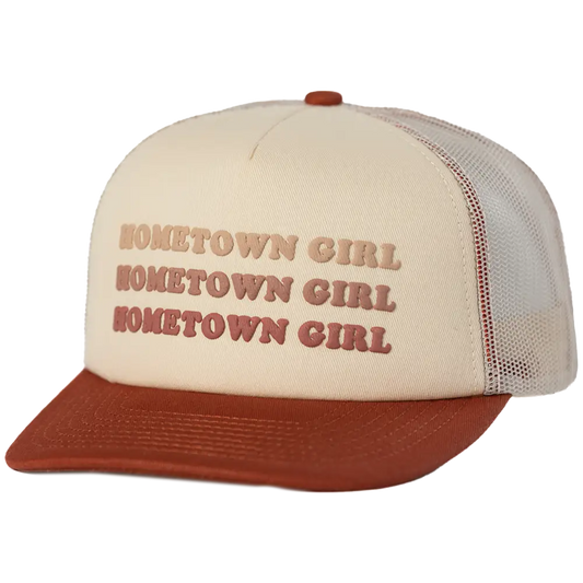Cream-colored trucker hat with a rust-brown brim and mesh back, featuring the phrase ’hometown girl’ embroidered in three stacked rows of matching rust-brown lettering.