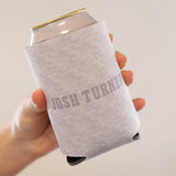 A light gray, textured fabric can cooler with a subtle pattern and the words ’josh turner’ printed in matching gray lettering.