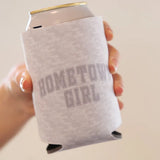 Gray camouflage-patterned can cooler with ’hometown girl’ printed in a faded gray collegiate-style font.